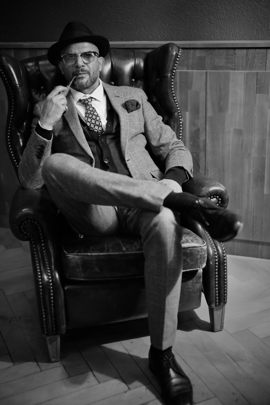 Barbiere con cappello, occhiali e abito in poltrona di pelle, bianco e nero – The Barber Zurigo